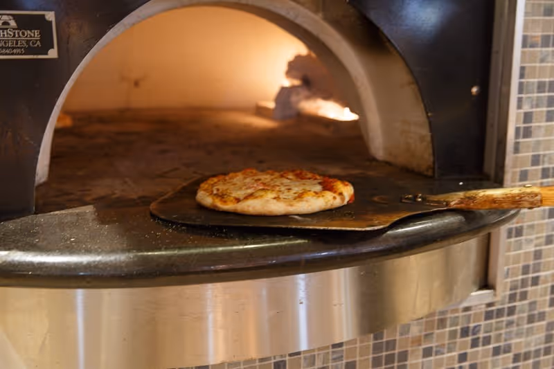 A small pizza on a peel being baked in a wood-fired pizza oven.