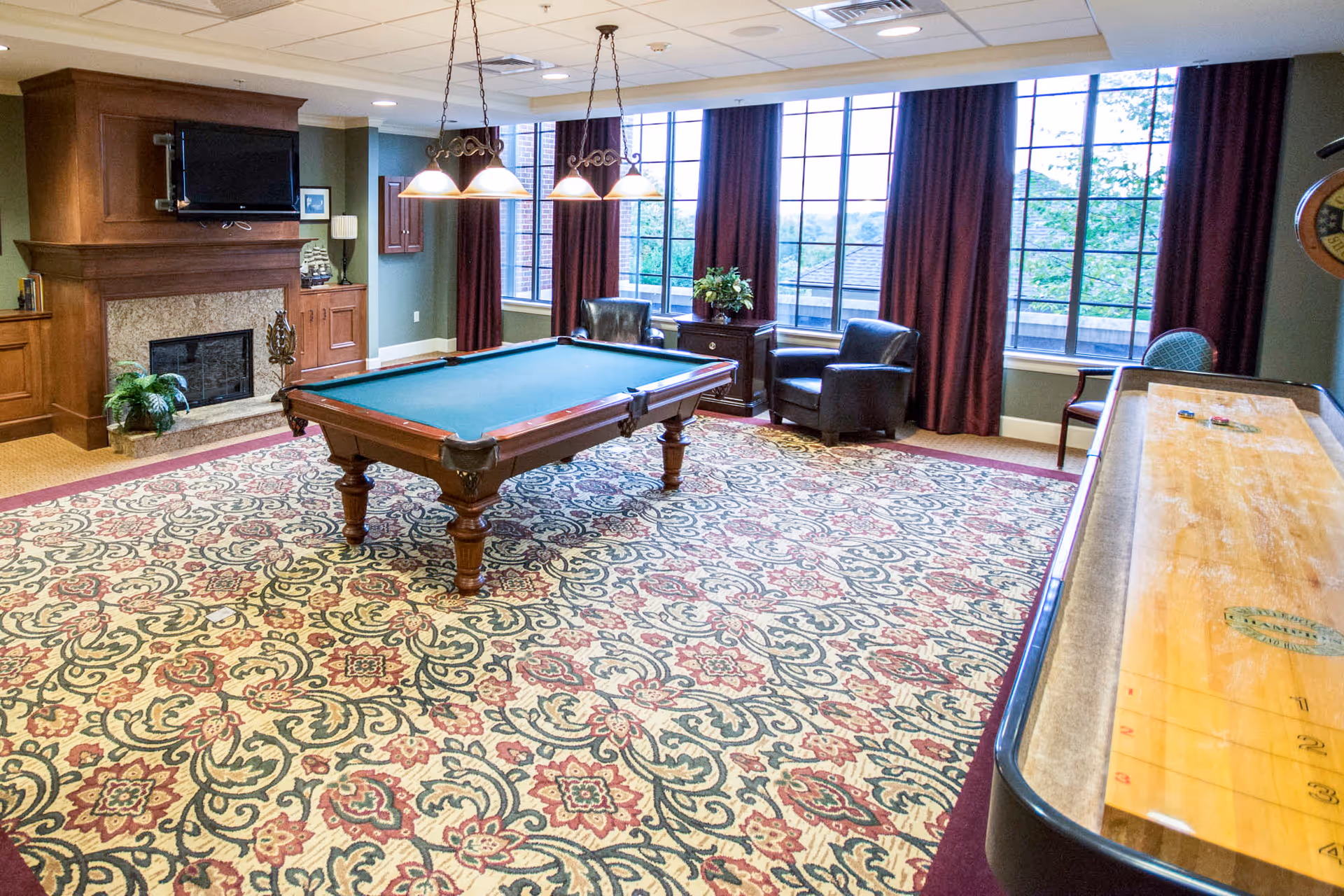 Spacious recreation room with a pool table, fireplace, seating, patterned carpet and large windows.