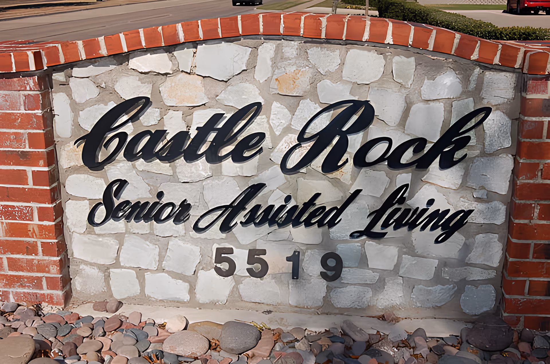 Stone and brick sign for Castle Rock Senior Assisted Living with the number 5519 below the name, surrounded by rocks at the base.