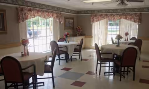 Sunlit dining room in a senior facility with round tables and empty chairs.