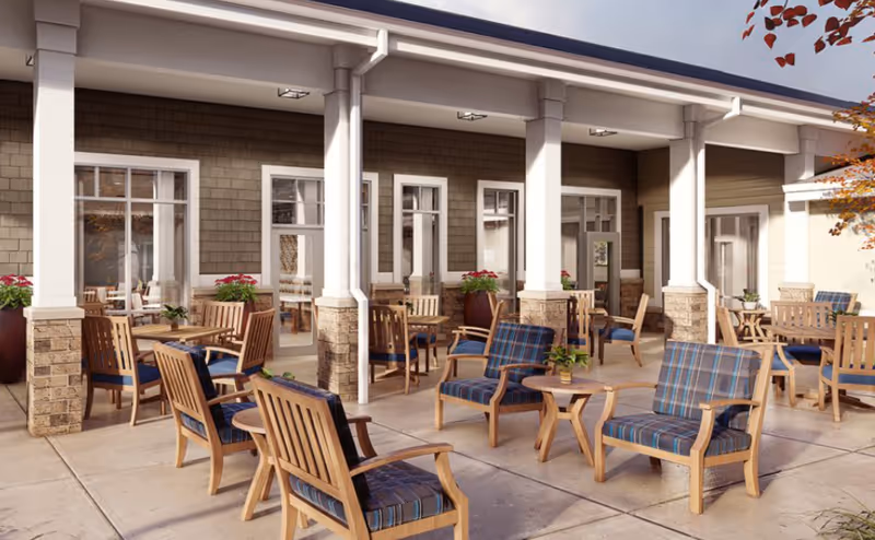 Outdoor patio area with multiple wooden chairs and tables, some with blue plaid cushions, potted plants, and a building with large windows and white pillars in the background.