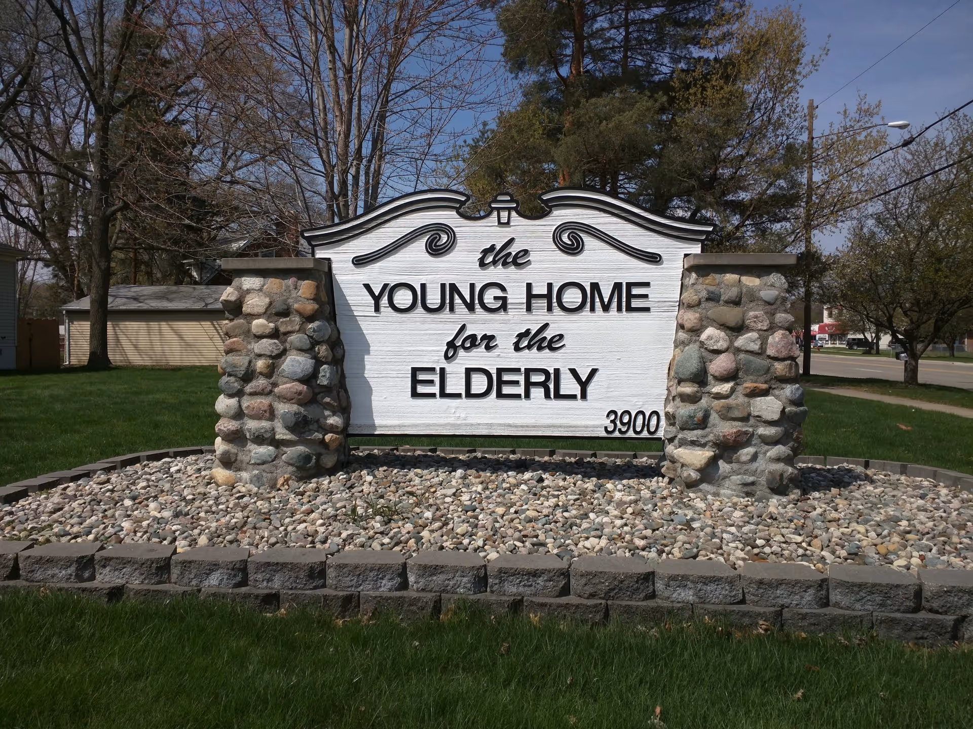 A freestanding stone-and-wood sign reading "The Young Home for the Elderly" with the address 3900 on a grassy lawn.