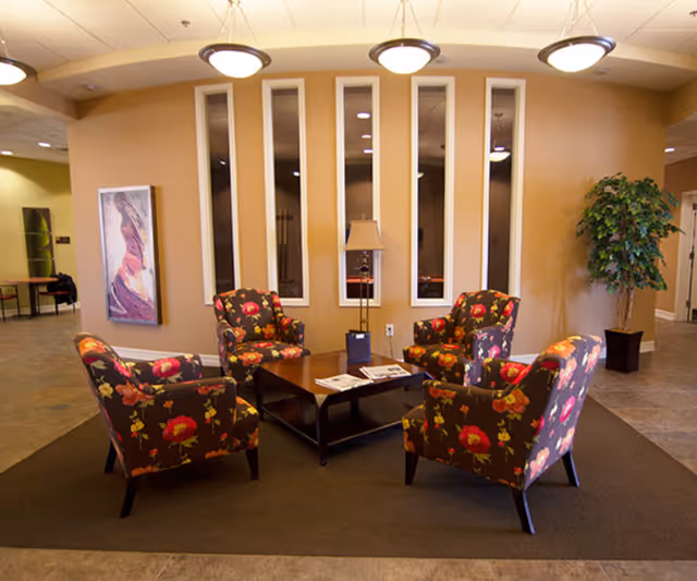 Seating area with four floral armchairs around a coffee table in a warmly lit senior living facility lobby.
