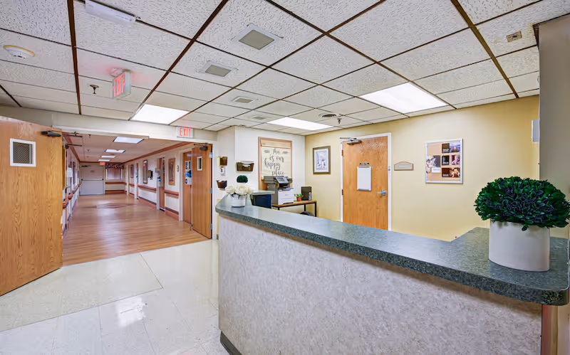 Reception desk and lobby area of a senior living facility with a hallway lined with doors.