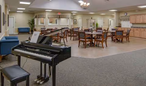 Piano in foreground with multiple tables and chairs in a spacious dining area.