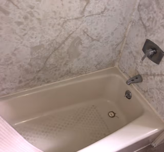 Beige bathtub with metal faucet in a marble-tiled bathroom.