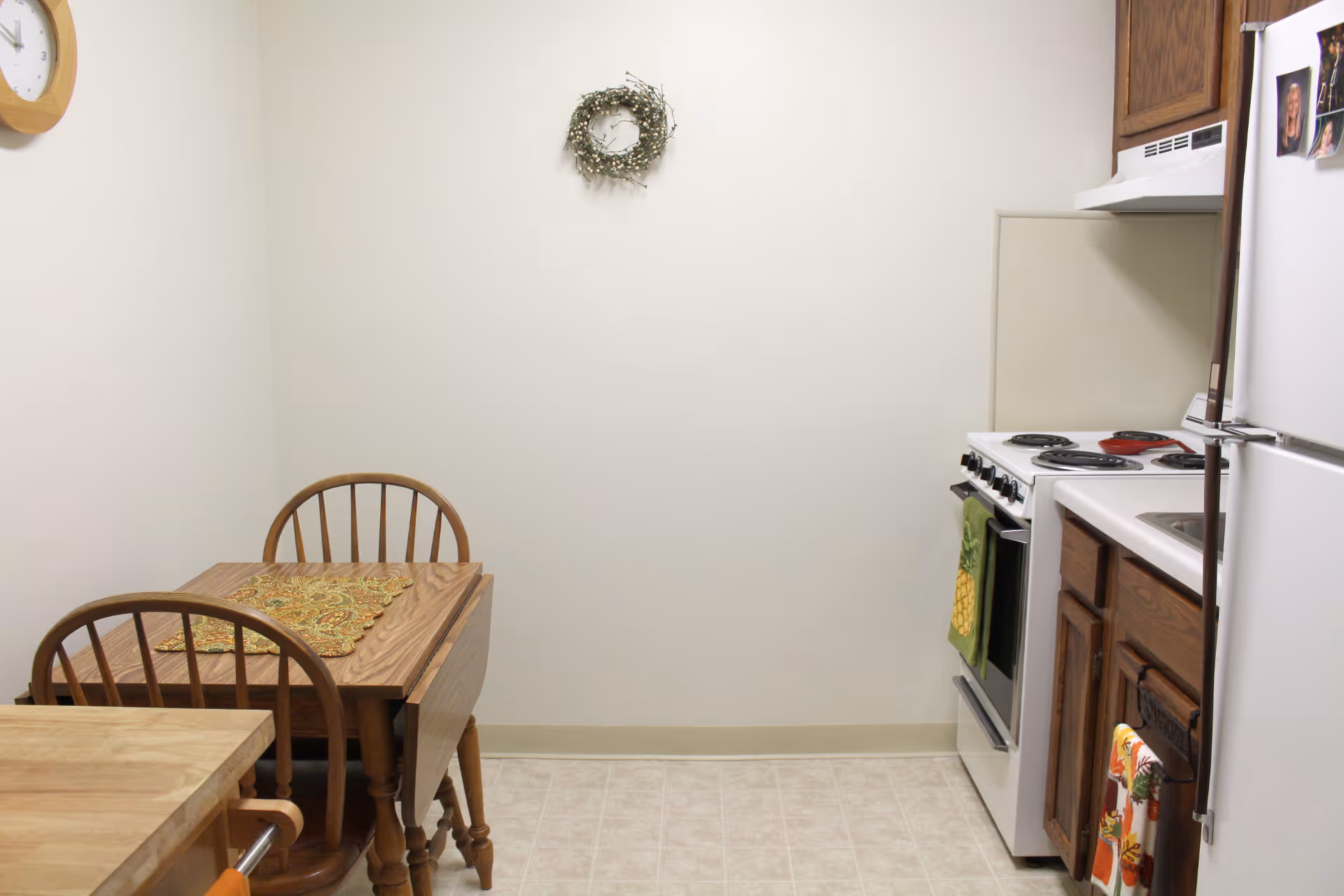 Small kitchen and dining nook with a wooden drop-leaf table and chairs, stove, refrigerator, and cabinets.