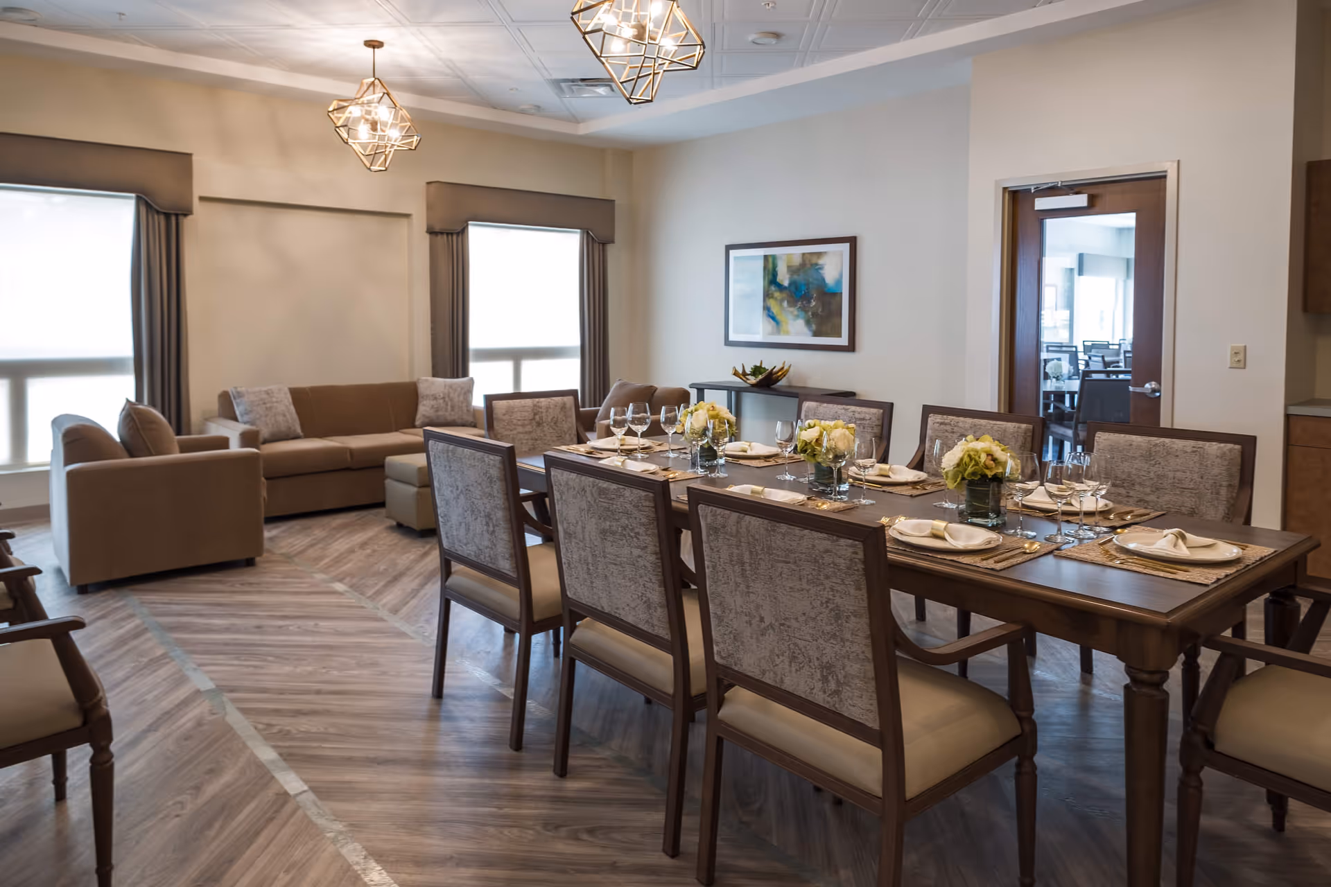 Communal dining room with a long wooden dining table set for a meal and an adjacent seating area with sofas and armchairs.