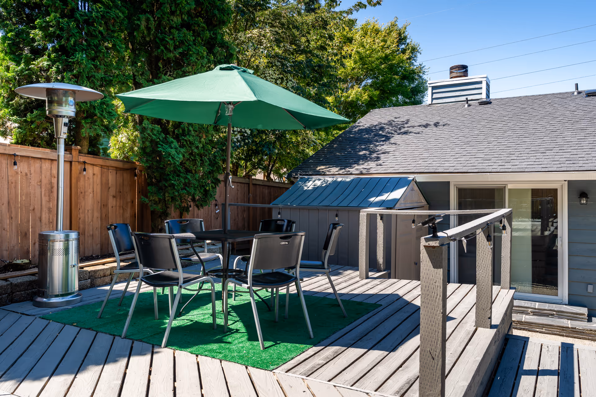 Outdoor wooden deck with a patio table and chairs under a green umbrella, a patio heater, and a sliding glass door to the house.