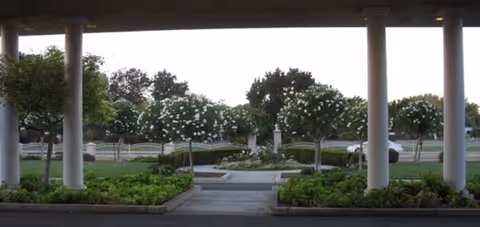 Covered entrance frames a courtyard with planters, trees, and a paved walkway.