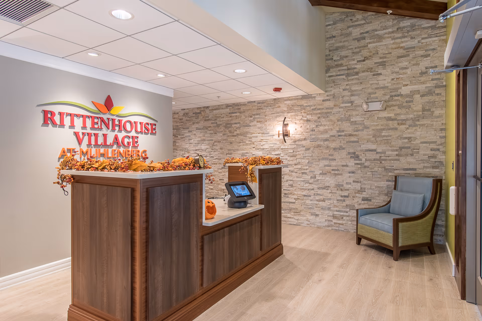 Reception desk and seating area in a senior living facility lobby with a 'Rittenhouse Village At Muhlenberg' sign on the wall.