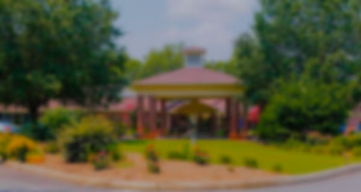 Blurry front exterior showing a covered entrance/gazebo, landscaped lawn, and trees.