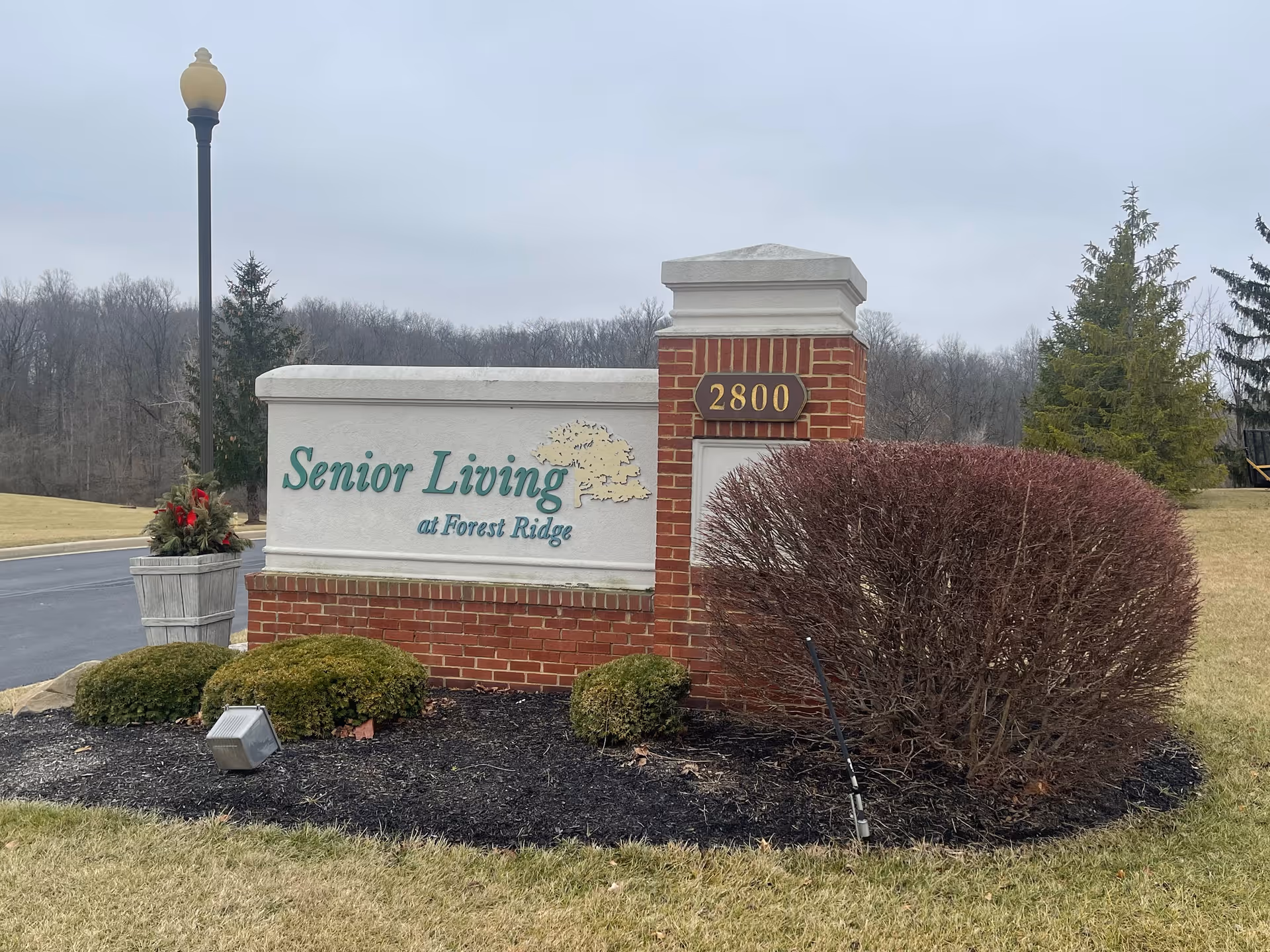 Brick entrance sign reading "Senior Living at Forest Ridge" with the address 2800, surrounded by landscaping and a lamppost.