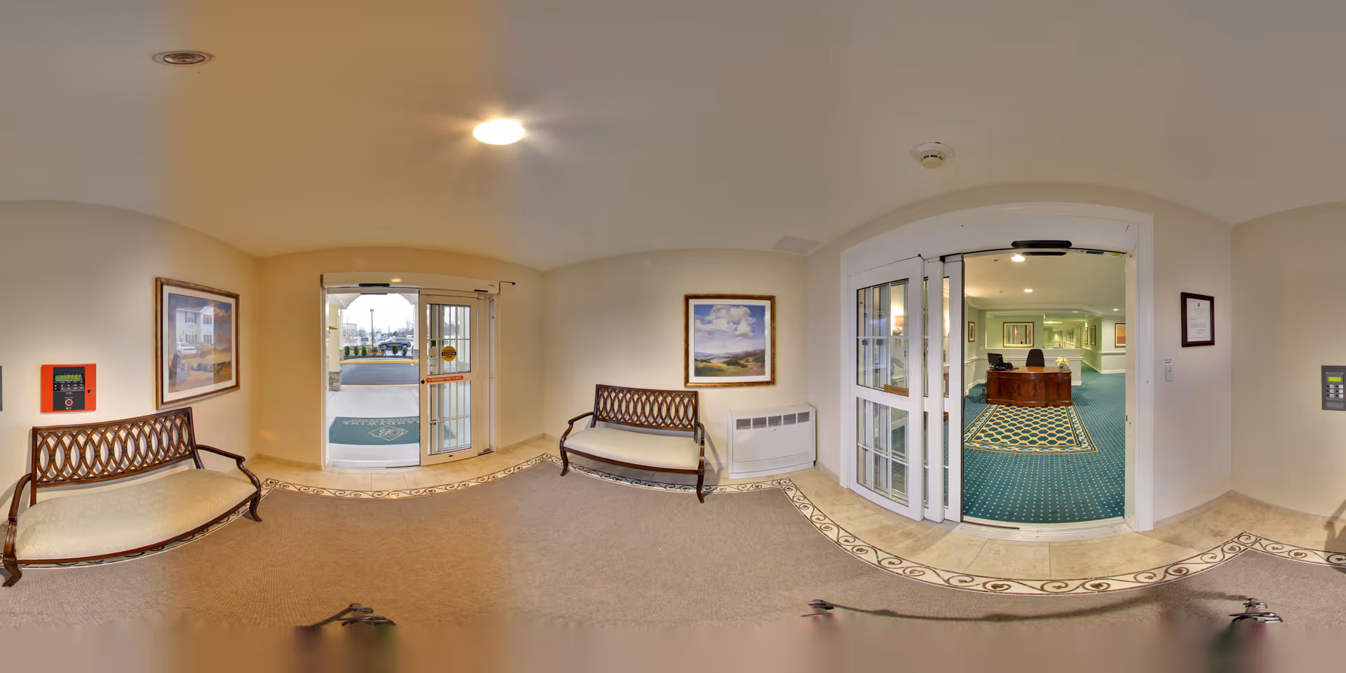 Entrance lobby with two benches, double glass doors leading outside, and an interior doorway opening to a reception area with green carpet.