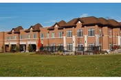 Exterior view of a two-story brick residential building with multiple windows and a manicured lawn in front under a clear blue sky.