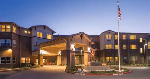 Exterior view of Carlton Senior Living Davis building at dusk with flagpole and entrance canopy.
