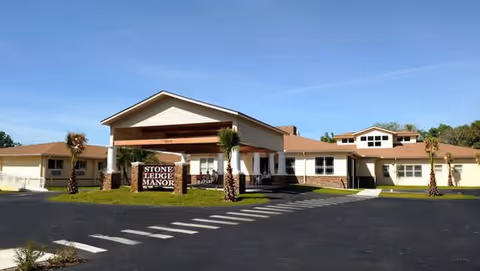 Front exterior view of Stone Ledge Manor Senior Living facility with a covered entrance, palm trees, and a sign displaying the facility name.