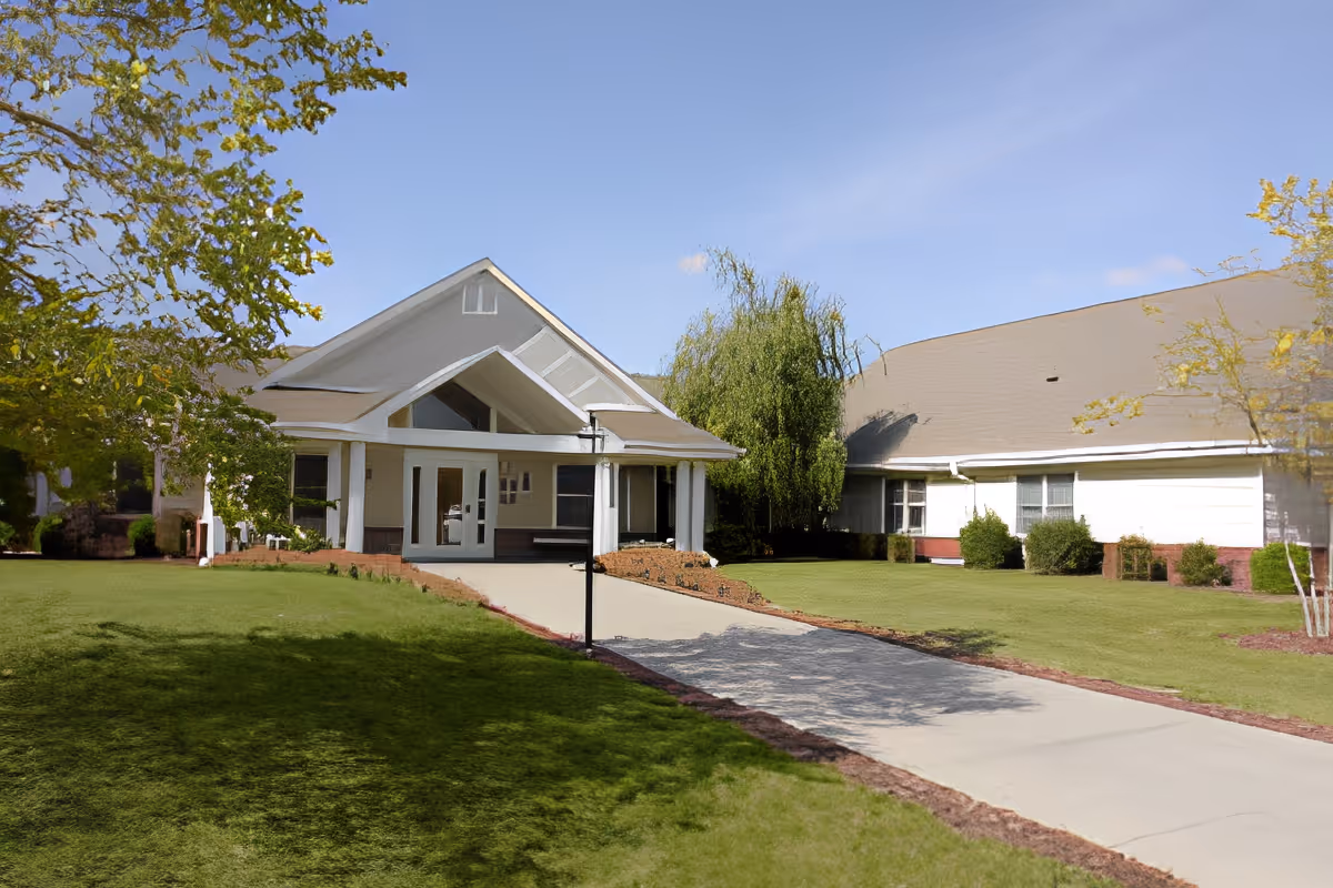 Front exterior view of Franciscan Villa building with a covered entrance, a paved driveway, green lawn, and trees under a clear blue sky.
