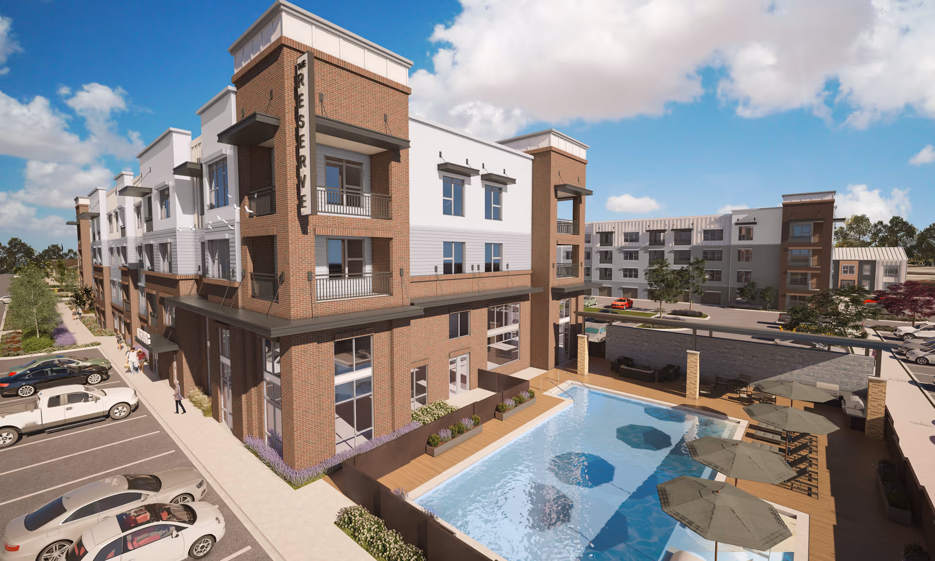 Exterior view of The Reserve at Woodland Lakes, a multi-story residential building with a brick and white facade. The image shows a swimming pool with umbrellas and lounge chairs on a wooden deck, adjacent to the building. Several parked cars and a few people walking are visible in the parking area beside the building under a partly cloudy sky.