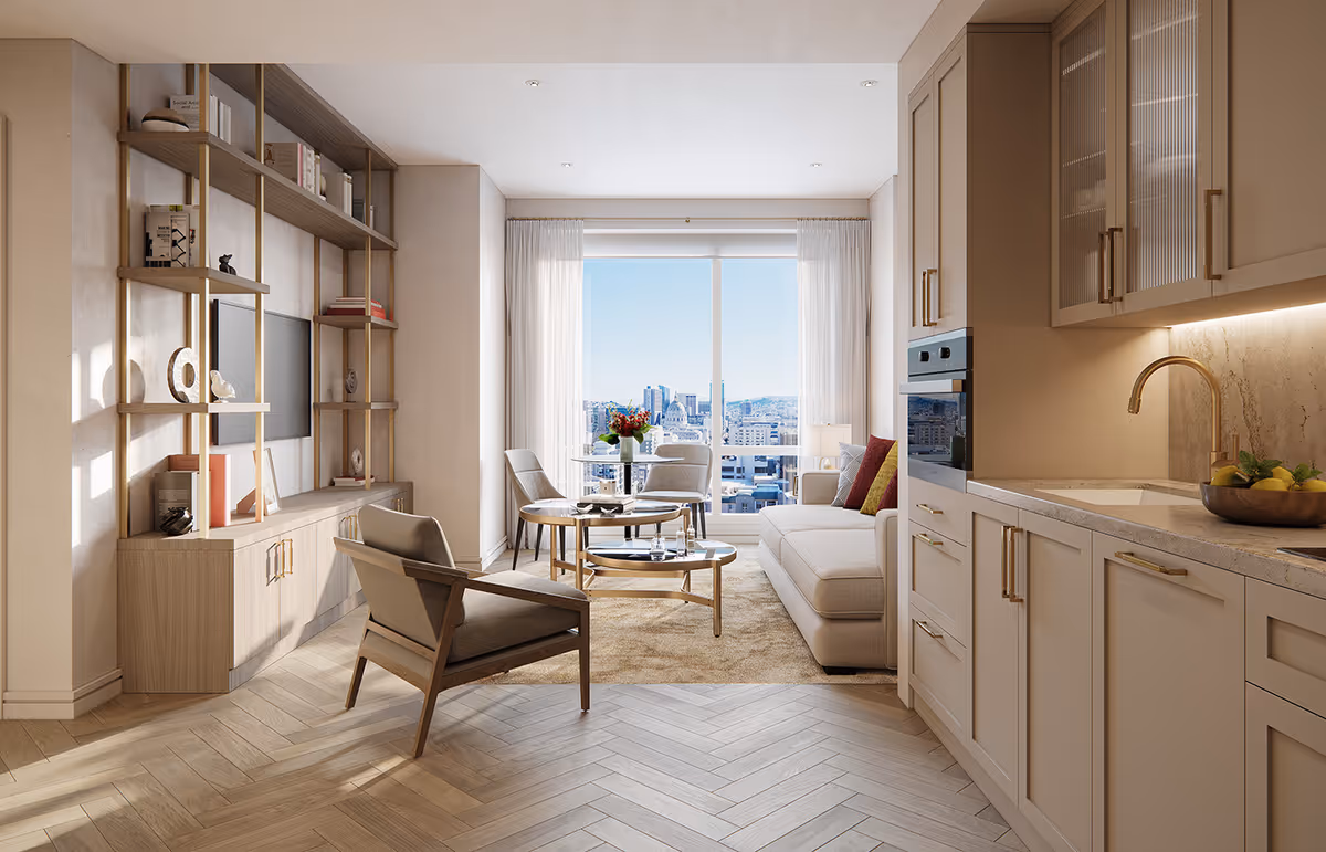 A bright and modern living area with a kitchen on the right featuring beige cabinets, a sink, and an oven. The living room has a beige sofa with colorful pillows, two chairs, and two round coffee tables on a light brown rug. A large window with sheer white curtains offers a cityscape view. On the left, there is a wooden shelving unit with decorative items and a mounted TV.