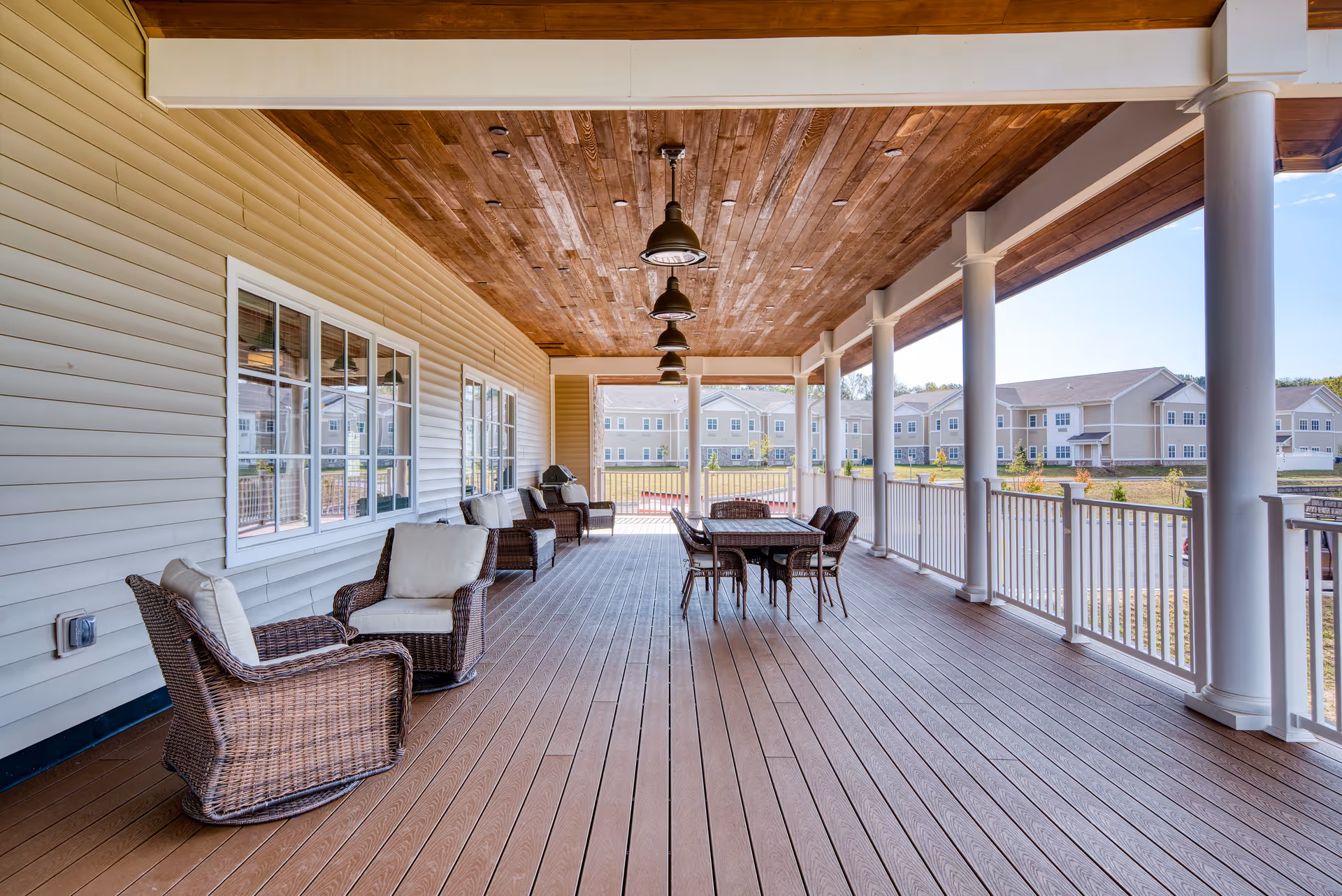 Covered outdoor porch with wicker chairs and a dining table overlooking the senior living complex.