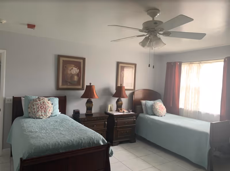 Bright shared bedroom with two twin beds, nightstands, lamps, and ceiling fan.