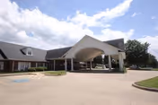 Exterior view of Brookridge Cove Rehab & Care facility showing a large covered entrance with a curved roof, a driveway with a handicap parking space, and a partly cloudy sky.