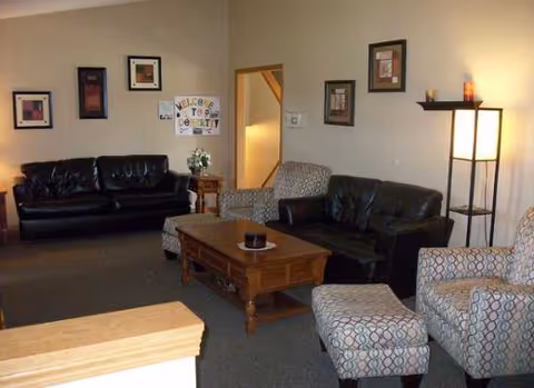 Cozy living room in a senior facility with black leather sofas and patterned chairs.