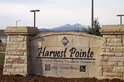 Stone entrance sign reading Harvest Pointe Senior Living with decorative pillars and distant mountains.