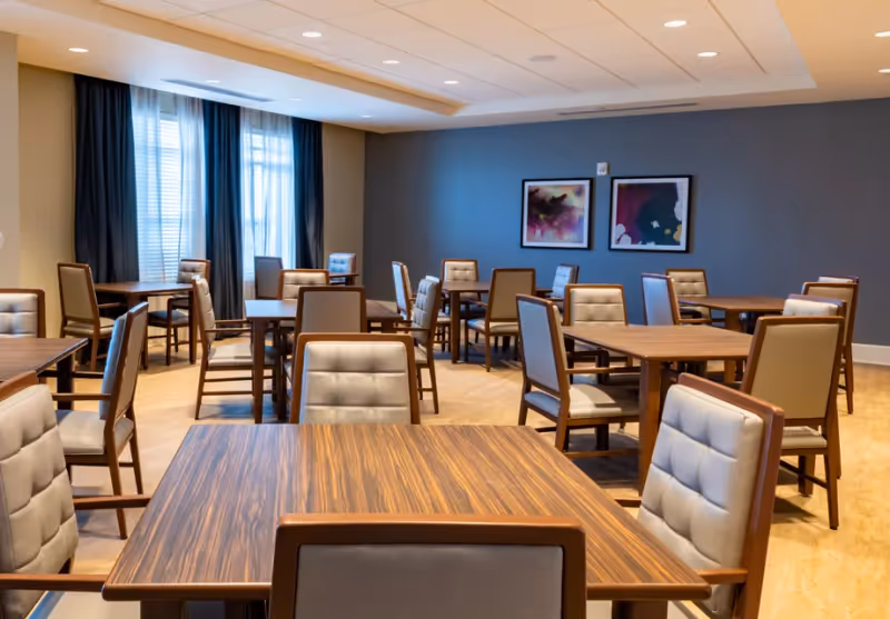 Bright communal dining room with wooden tables and cushioned chairs arranged throughout.