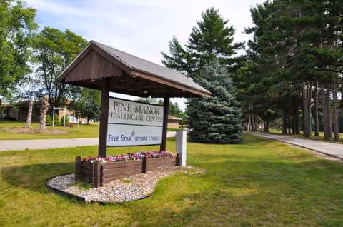 Sign for Pine Manor HealthCare Center amid trees and a grassy landscape.