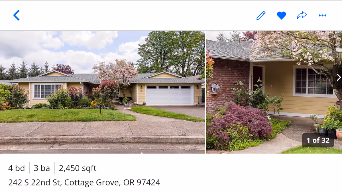 Exterior view of a single-story residential building with a well-maintained front yard featuring green grass, shrubs, and flowering trees. The house has a light yellow exterior with a two-car garage and a concrete driveway. The sky is partly cloudy.