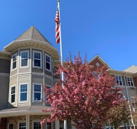 The Bel Rae Senior Living building facade with flagpole and pink flowering tree.