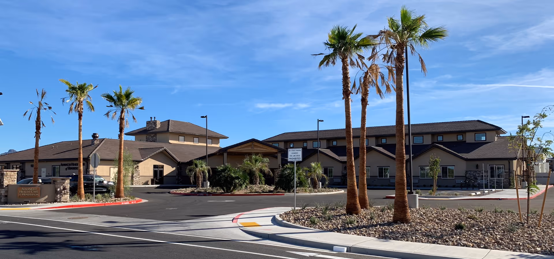 Exterior view of Advanced Health Care of Henderson facility with a clear blue sky, palm trees, and a paved driveway leading to the building entrance.