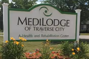 Large outdoor sign reading "Medilodge of Traverse City, A Health and Rehabilitation Center" with flowers and greenery in front.