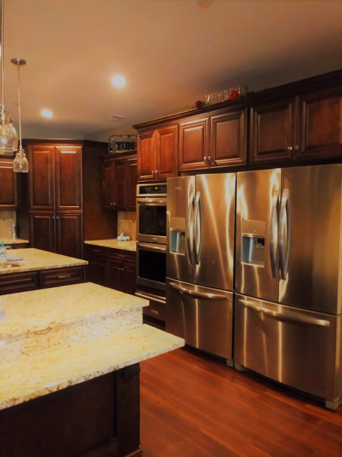Spacious kitchen with granite islands, dark wood cabinets and two stainless steel French-door refrigerators.