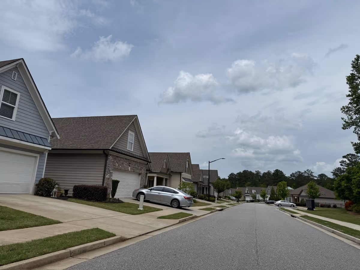 Wide view of a suburban street lined with single-family homes, driveways, and parked cars under an overcast sky.