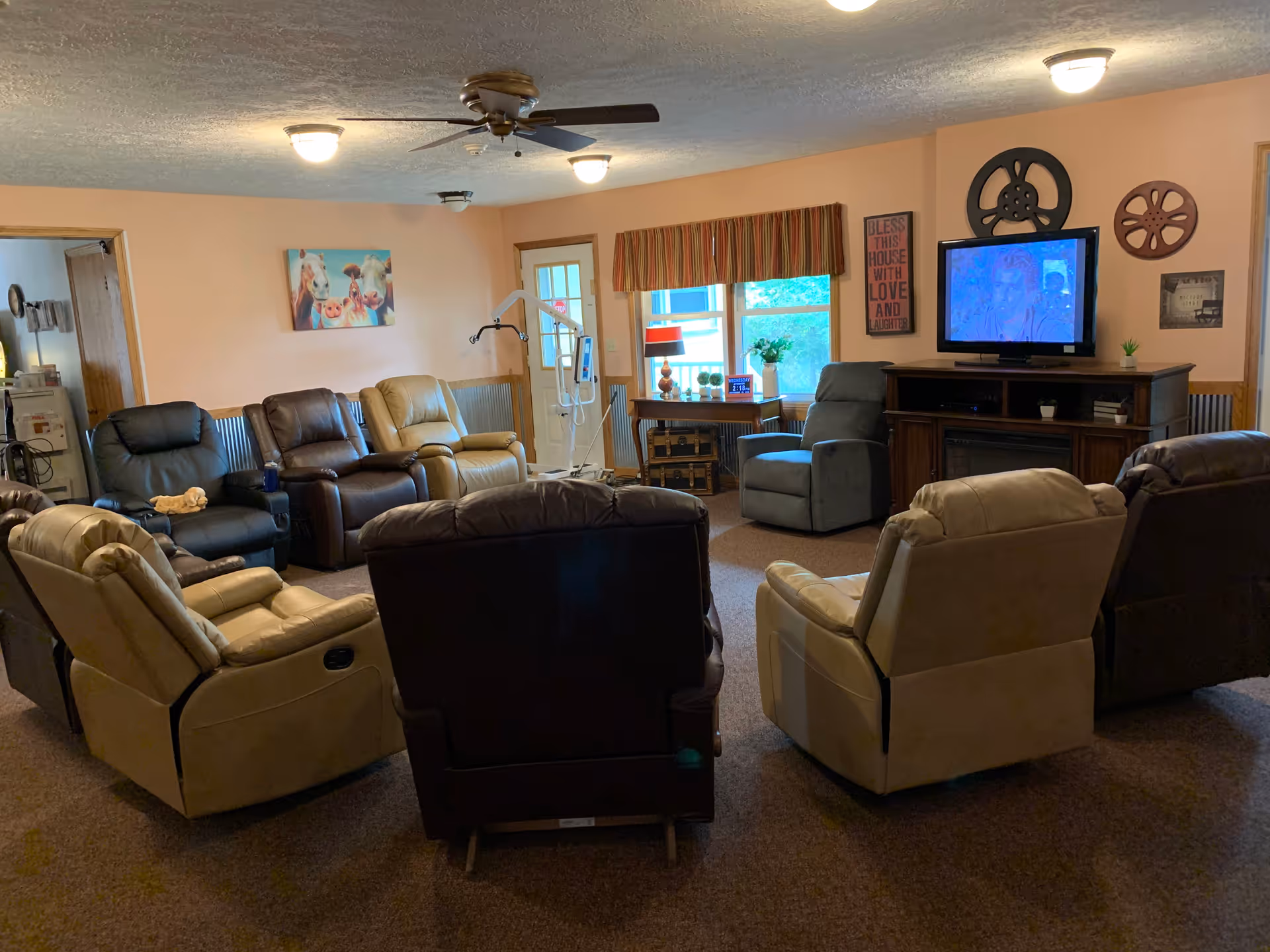 Communal living room with multiple recliners arranged facing a television and windows.