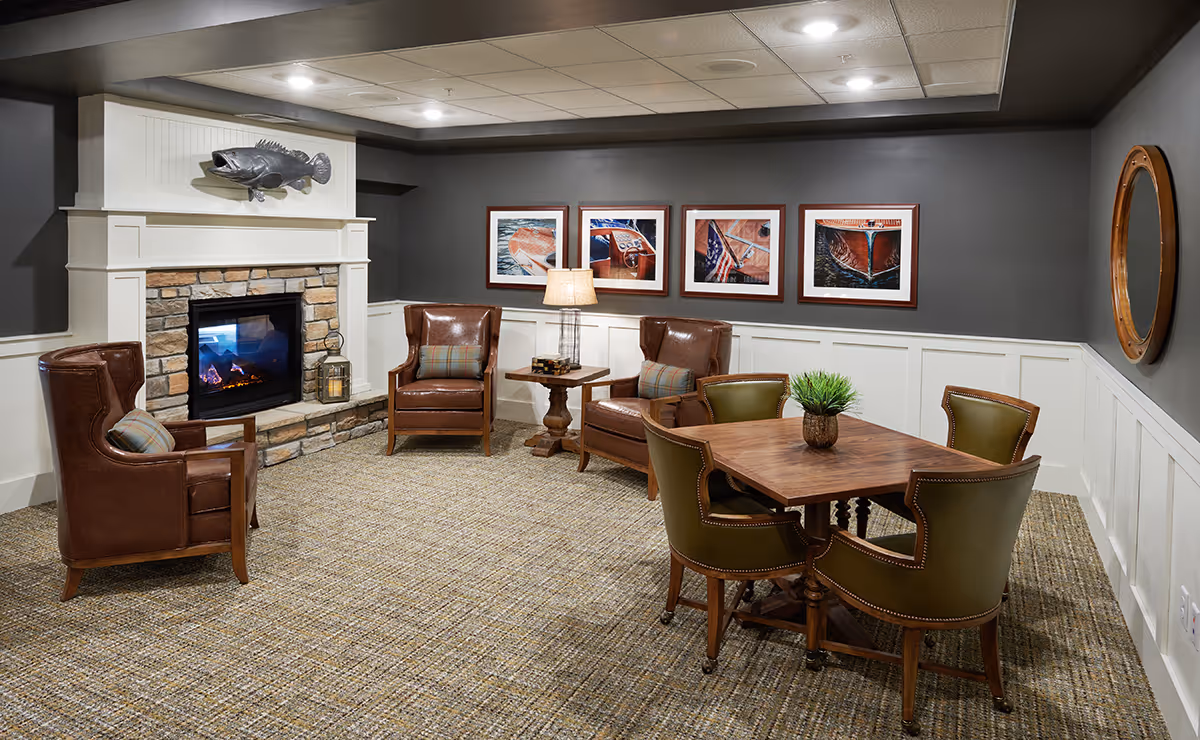 Cozy communal living room featuring a stone fireplace, leather armchairs, framed artwork, and a wooden table with four chairs.