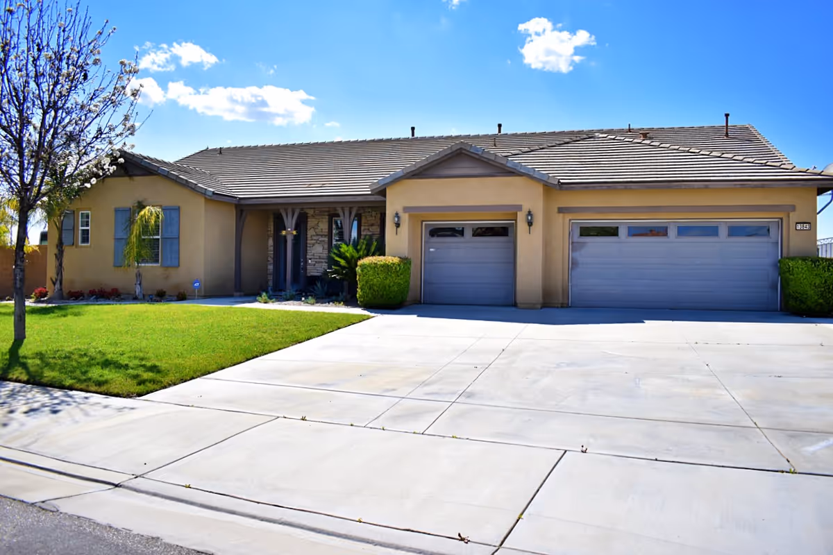 Single-story suburban house with a three-car garage, driveway, and front lawn under a blue sky.