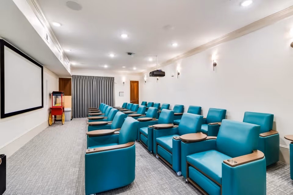 A small screening room with rows of teal recliner chairs facing a large projection screen and a popcorn cart at the front.