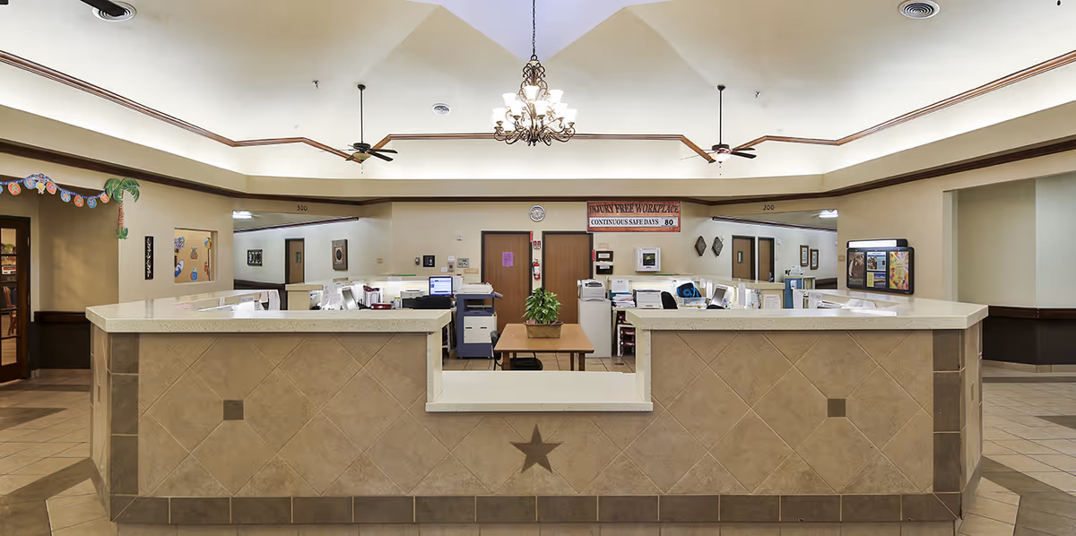 Tiled nurse station/reception desk in a well-lit interior lobby with computers, a chandelier, and ceiling fans.