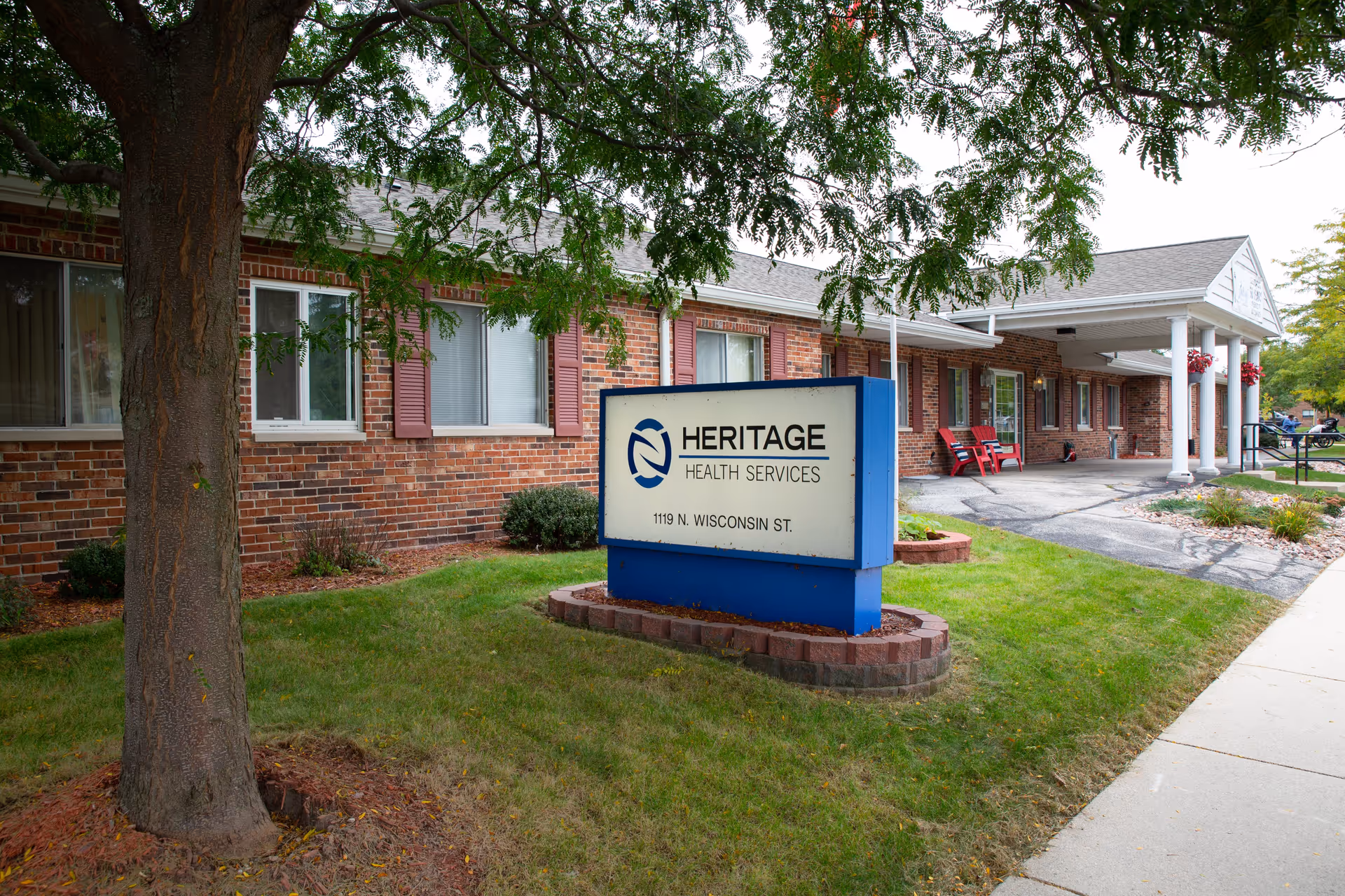 Front exterior of the Heritage Health Services building with a lawn and a freestanding sign by the sidewalk.