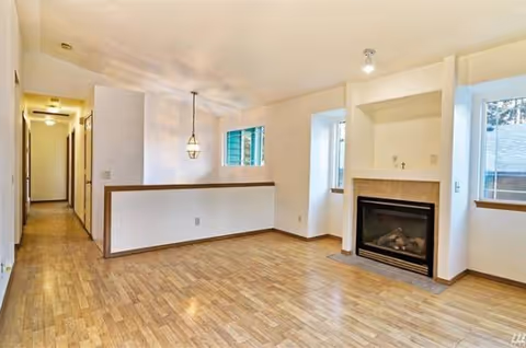 Bright living room with fireplace, wood floors, windows, and a partial half-wall divider.