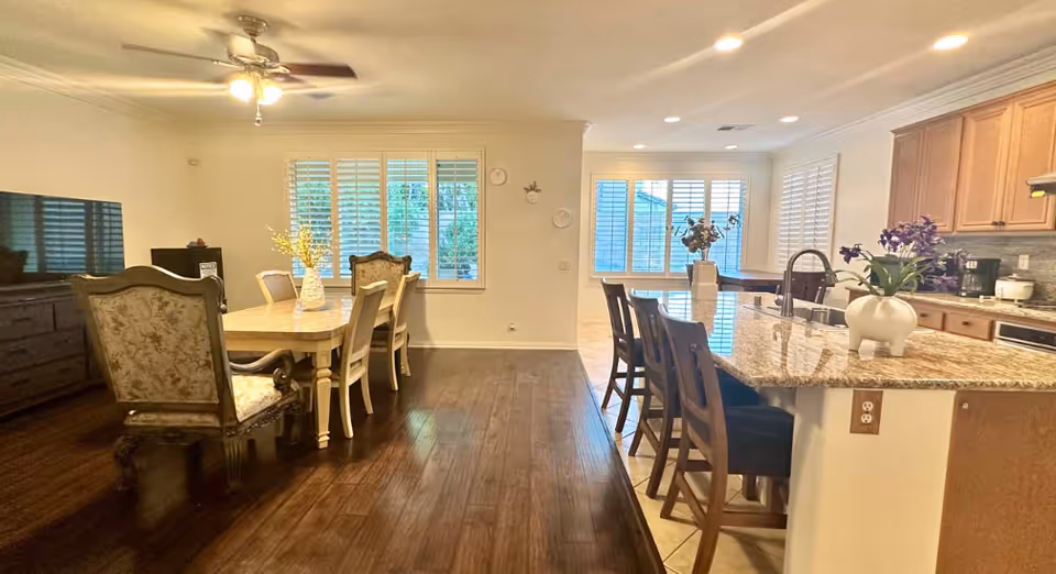 Open-concept dining and kitchen area with a formal dining table and chairs on dark hardwood and a granite-topped island with bar stools.