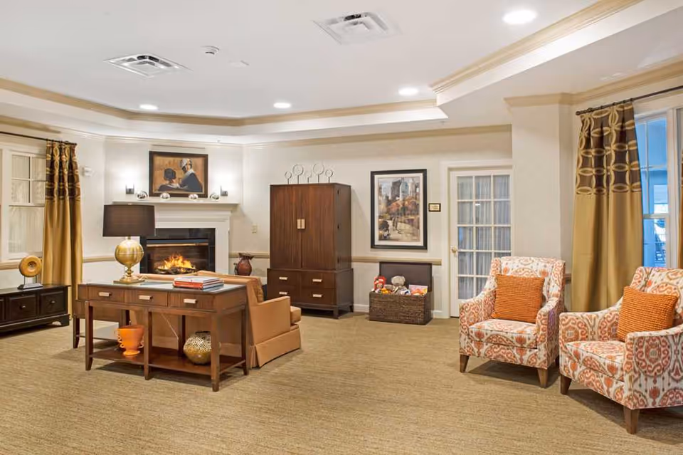 Well-lit communal living room with a fireplace, seating, decorative chairs, and cabinetry.