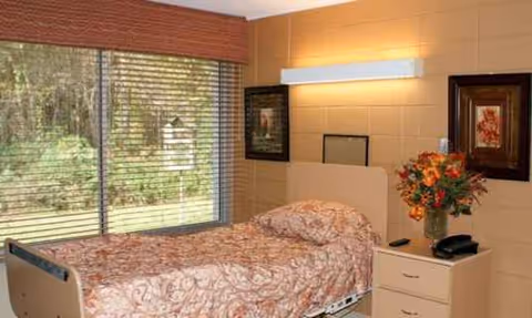 A patient bedroom with floral bedding, a dresser, and a vase of flowers.