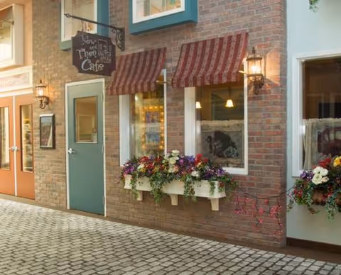 Brick building exterior with striped awnings, display windows, and flower boxes along a cobblestone street.
