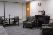 Lounge area with patterned chairs, small table, fireplace, and floral decor in a nursing facility.