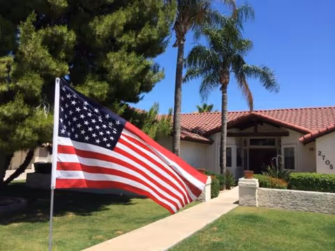 American flag in front of a single-story senior living facility with palm trees.